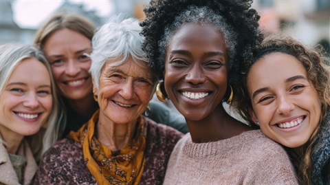 Five smiling women of different ages and backgrounds pose together outdoors, looking at the camera. AI-generated image for illustrative purposes only.jpeg