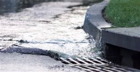 Photo of water along street curb flowing into street storm drain