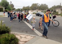Photograph of a group of children and crossing guard crossing residential street and woman on bike